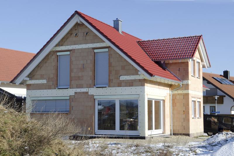 Rohbau eines Einfamilienhauses mit rotem Satteldach und weißen Fenstern