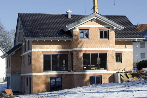 Zweigeschossiges Einfamilienhaus im Rohbau mit dunklem Dach im Schnee